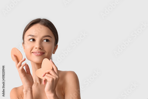 Pretty young woman with makeup sponges on grey background