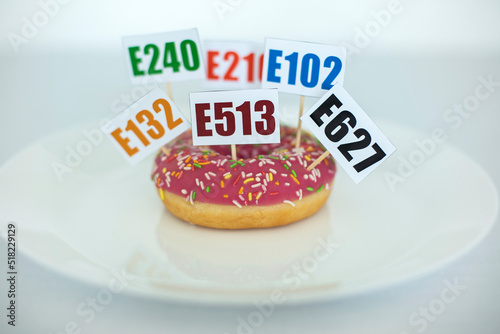 Fotografie Plate with Donut with Cards with Names of Harmful Additive Chemicals Stuck in it
