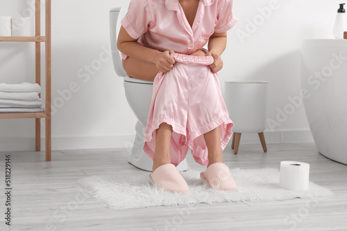 Mature woman with diarrhea sitting on toilet bowl in bathroom photo