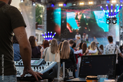 low light, professional DJ music mixer, laptop at party festival with crowd of people in background