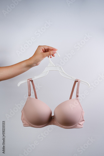 A young woman is holding a hanger with a bra. Closeup. Front view.