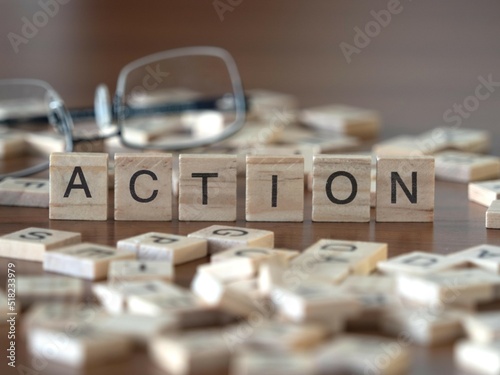 action word or concept represented by wooden letter tiles on a wooden table with glasses and a book photo