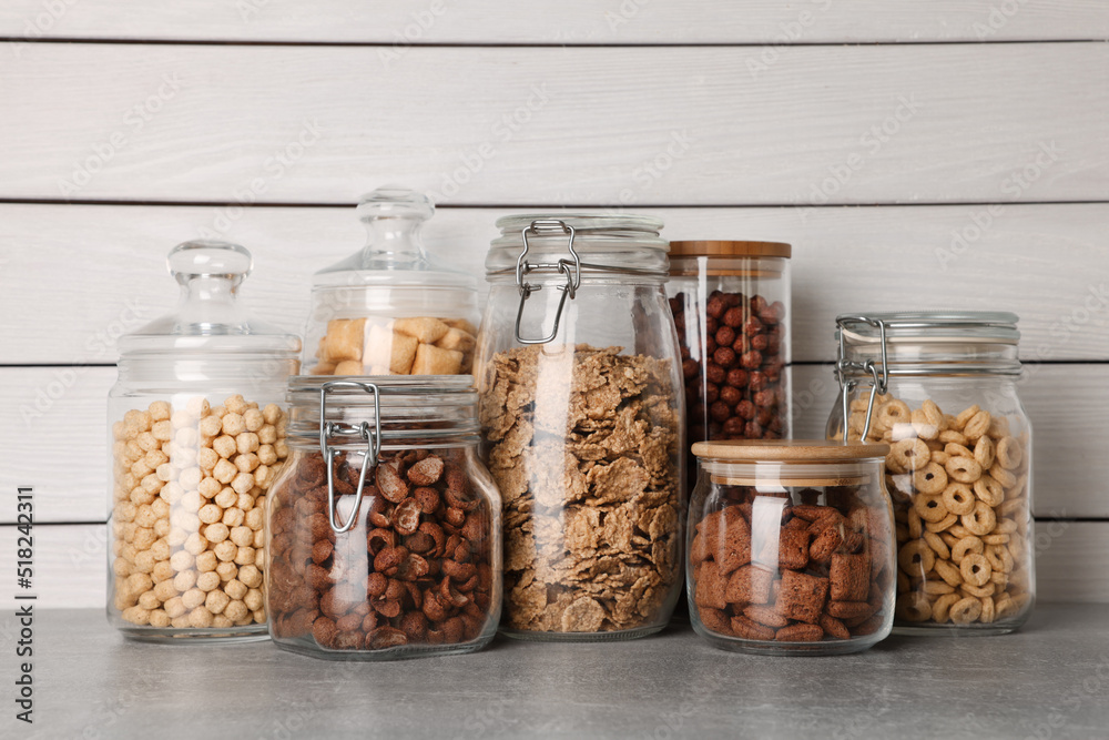 Glass containers with different breakfast cereals on grey countertop near white wooden wall Glass containers with different breakfast cereals on grey countertop near white wooden wall