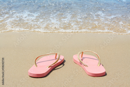 Stylish pink flip flops on sandy beach near sea