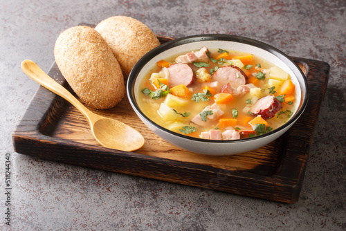 Portion of hot pea soup with potatoes, onions, carrots, bacon and sausages close-up in a bowl on the table. Horizontal photo