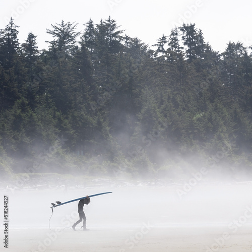 Young surfer walking with his surfboard in the mist on Chesterman beach near Tofino, Vancouver Island, British Columbia, Canada. photo