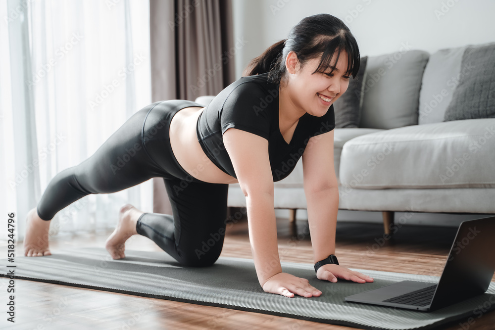 Asian chubby woman sitting on the floor in living room practice online yoga lesson with the computer. female having meditate training class on the laptop.. Asian chubby woman sitting on the floor in living room practice online yoga lesson with the computer. female having meditate training class on the laptop..