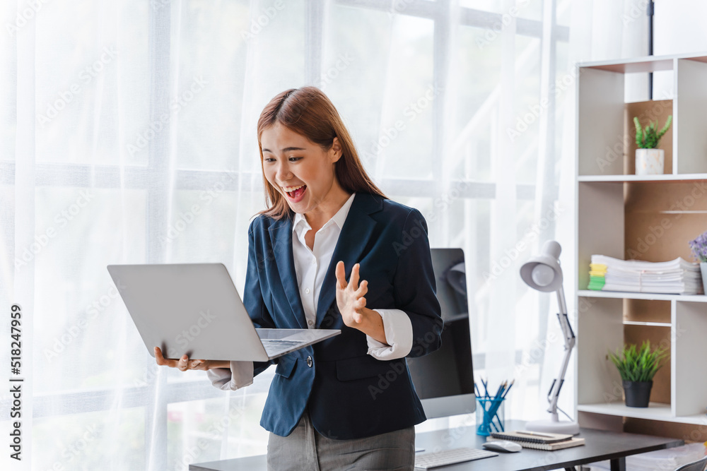 Excited shocked pretty young Asian business woman feeling happy while standing in modern office, holding and using laptop. Excited shocked pretty young Asian business woman feeling happy while standing in modern office, holding and using laptop.