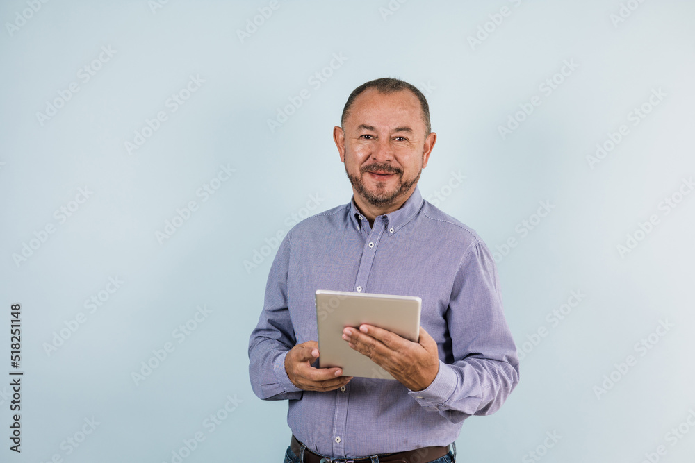 portrait of hispanic senior man wearing casual clothes and holding a tablet on blue background in Mexico Latin America portrait of hispanic senior man wearing casual clothes and holding a tablet on blue background in Mexico Latin America