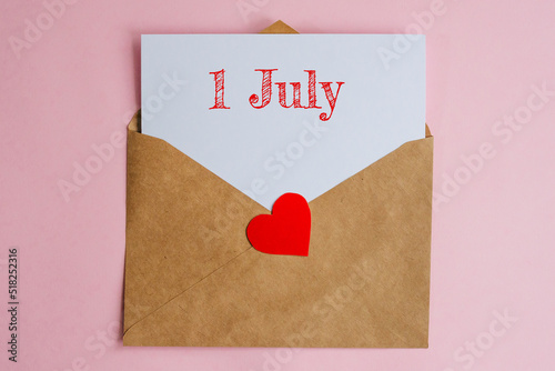Kraft envelope with a white sheet of paper and a date 1 july, with a red heart. Flat lay on pink background, romance and love concept