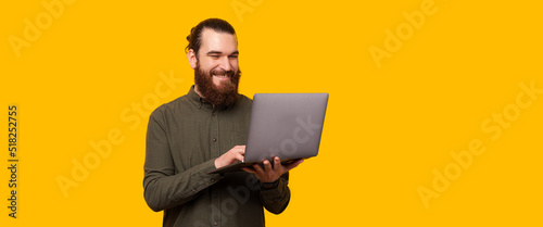 Fotografia A happy bearded man is typing in his laptop near a free and yellow copy space