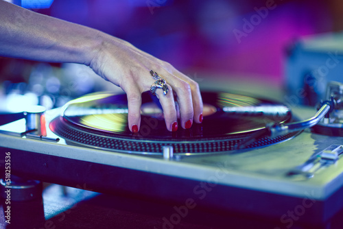 Detail of a woman's hand scratching a classic vinyl record in a nightclub.