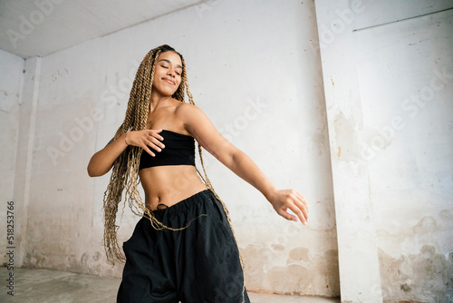 Mixed race girl with long blonde braids dancing in a black tracksuit in an abandoned warehouse while smiling and enjoying her passion and exercise.