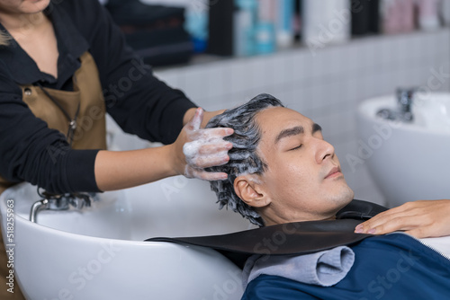 Asian attractive young male get hair washed by hairdresser in salon. Professional hair stylist woman give service and hair wash and massage to handsome man customer lying down on salon washing bed. photo