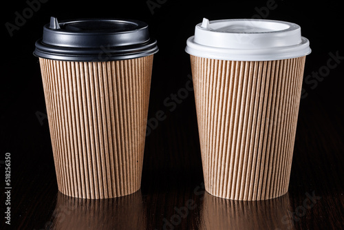 Brown paper cup for hot coffee, tea, drinks with black and white lids on a black background. Angle view.