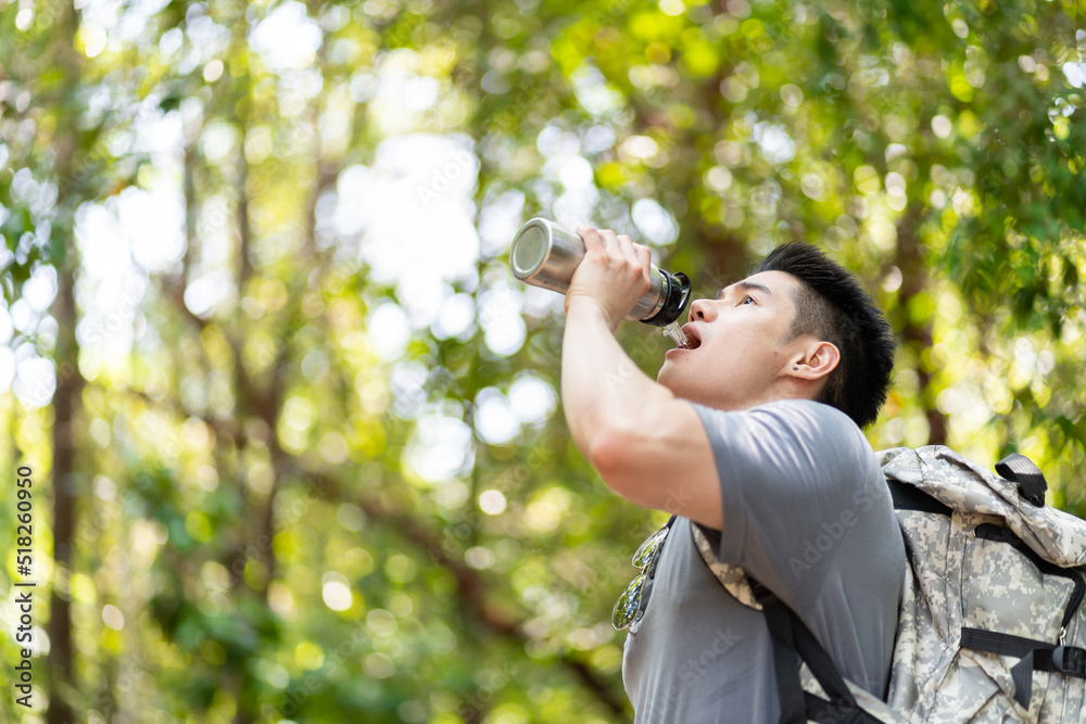 Asian handsome man backpacker drinking bottle of water in forest pack. Attractive young male traveler traveling alone and sip water while walking in nature wood with happiness during vacation trip. Asian handsome man backpacker drinking bottle of water in forest pack. Attractive young male traveler traveling alone and sip water while walking in nature wood with happiness during vacation trip.