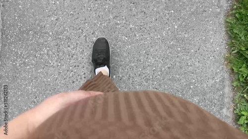 View from above of pregnant woman walking on the street. Close-up of pregnant woman wearing a casual cotton dress and sneakers, holding a hand on her belly while walking.
