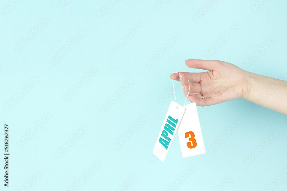 April 3rd. Day 3 of month, Calendar date. Hand hold price tag with calendar date on blue background. Spring month, day of the year concept. April 3rd. Day 3 of month, Calendar date. Hand hold price tag with calendar date on blue background. Spring month, day of the year concept.