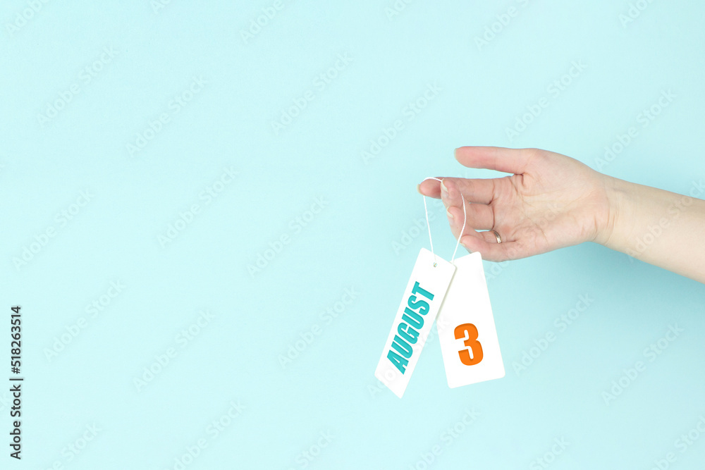August 3rd. Day 3 of month, Calendar date. Hand hold price tag with calendar date on blue background. Summer month, day of the year concept. August 3rd. Day 3 of month, Calendar date. Hand hold price tag with calendar date on blue background. Summer month, day of the year concept.