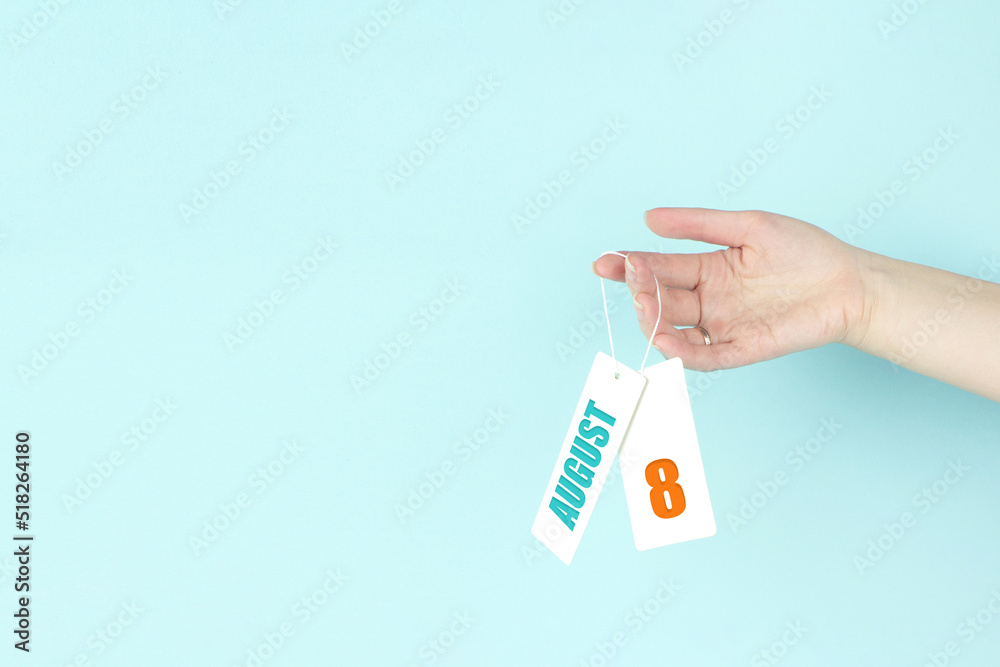 August 8th. Day 8 of month, Calendar date. Hand hold price tag with calendar date on blue background. Summer month, day of the year concept. August 8th. Day 8 of month, Calendar date. Hand hold price tag with calendar date on blue background. Summer month, day of the year concept.