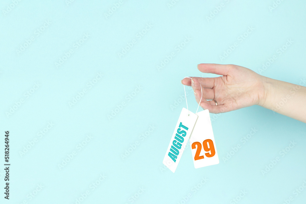 August 29th. Day 29 of month, Calendar date. Hand hold price tag with calendar date on blue background. Summer month, day of the year concept. August 29th. Day 29 of month, Calendar date. Hand hold price tag with calendar date on blue background. Summer month, day of the year concept.