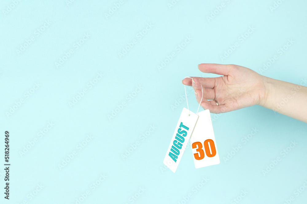 August 30th. Day 30 of month, Calendar date. Hand hold price tag with calendar date on blue background. Summer month, day of the year concept. August 30th. Day 30 of month, Calendar date. Hand hold price tag with calendar date on blue background. Summer month, day of the year concept.