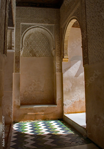 Sunlit doorway with light splashing over a  floor of tiles in blue, green and white. A zig zag pattern and rounded archways add to this picture of contrasts. A backdrop of a shadowed alcove. photo