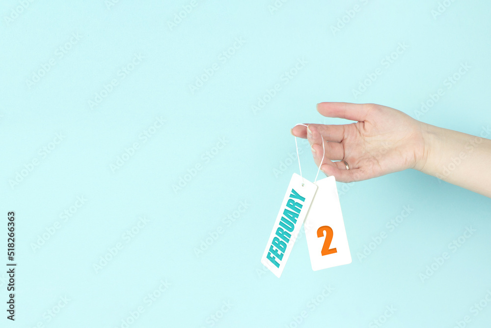 February 2nd. Day 2 of month, Calendar date. Hand hold price tag with calendar date on blue background. Winter month, day of the year concept. February 2nd. Day 2 of month, Calendar date. Hand hold price tag with calendar date on blue background. Winter month, day of the year concept.
