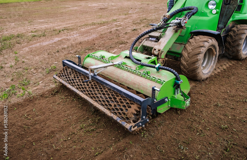 Mini skid steer loader clear the construction site. Land work by the territory improvement. Small tractor with a rotary cultivator attachment and ground leveler for moving soil. Agriculture machine photo