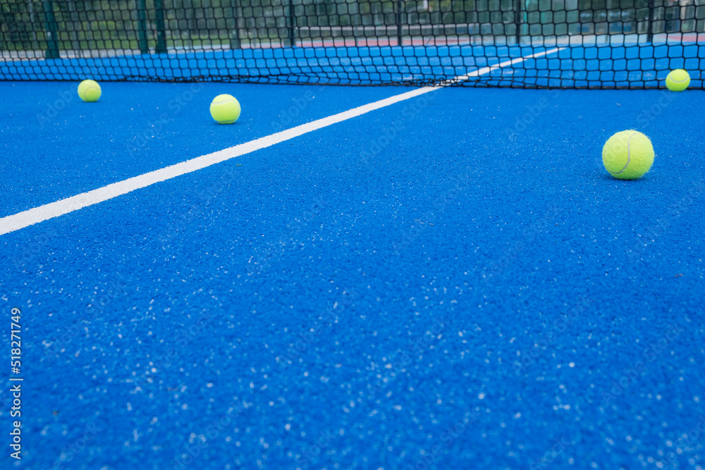 Selective focus. Blue paddle tennis court with synthetic grass and several yellow balls