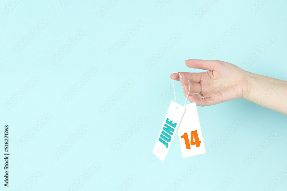 June 14th. Day 14 of month, Calendar date. Hand hold price tag with calendar date on blue background. Summer month, day of the year concept. June 14th. Day 14 of month, Calendar date. Hand hold price tag with calendar date on blue background. Summer month, day of the year concept.