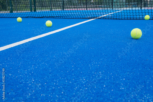 Selective focus. Blue paddle tennis court with synthetic grass and several yellow balls © Vic