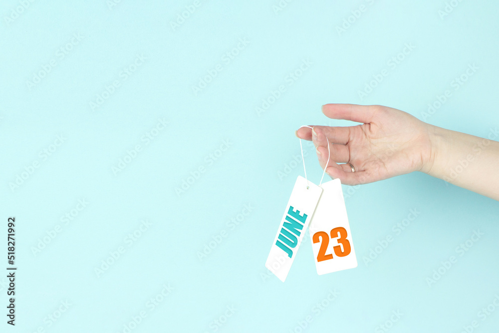 June 23rd. Day 23 of month, Calendar date. Hand hold price tag with calendar date on blue background. Summer month, day of the year concept. June 23rd. Day 23 of month, Calendar date. Hand hold price tag with calendar date on blue background. Summer month, day of the year concept.