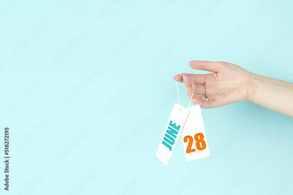June 28th. Day 28 of month, Calendar date. Hand hold price tag with calendar date on blue background. Summer month, day of the year concept. June 28th. Day 28 of month, Calendar date. Hand hold price tag with calendar date on blue background. Summer month, day of the year concept.
