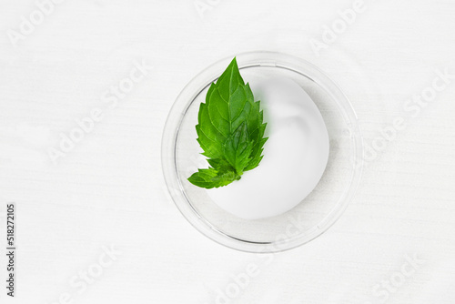 A smear of cosmetic white cream on a white wooden table with green mint leaves. Body lotion, body and skin care product with natural ingredients.