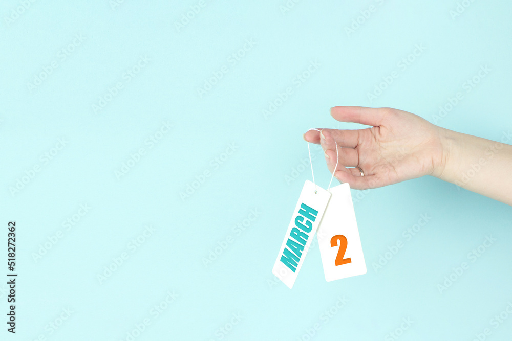 March 2nd. Day 2 of month, Calendar date. Hand hold price tag with calendar date on blue background. Spring month, day of the year concept. March 2nd. Day 2 of month, Calendar date. Hand hold price tag with calendar date on blue background. Spring month, day of the year concept.
