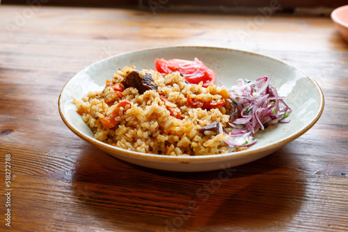 Pilaf with rice and beef or lamb, tomato and marinated red onion on plate on wooden table. Lifestyle, selective focus