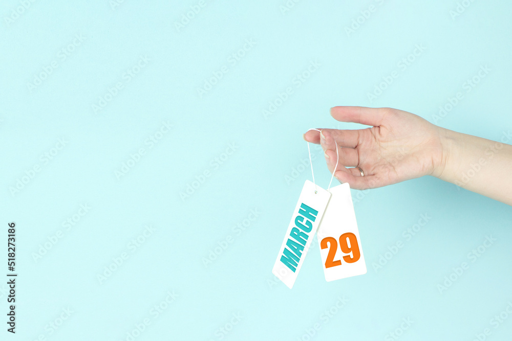 March 29th. Day 29 of month, Calendar date. Hand hold price tag with calendar date on blue background. Spring month, day of the year concept. March 29th. Day 29 of month, Calendar date. Hand hold price tag with calendar date on blue background. Spring month, day of the year concept.
