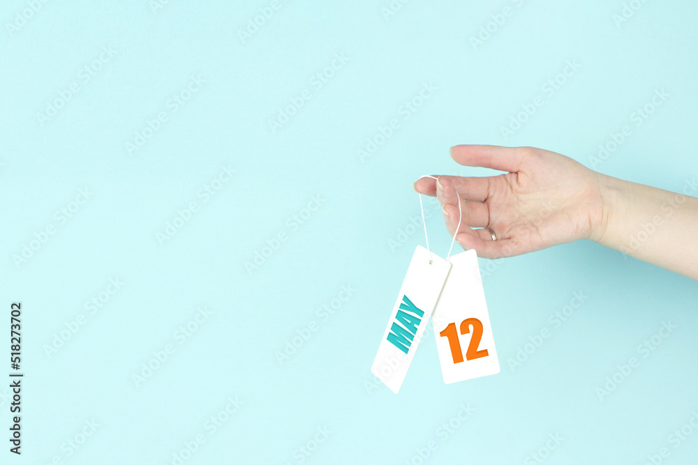 May 12nd. Day 12 of month, Calendar date. Hand hold price tag with calendar date on blue background. Spring month, day of the year concept. May 12nd. Day 12 of month, Calendar date. Hand hold price tag with calendar date on blue background. Spring month, day of the year concept.