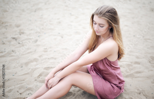 Young woman in pink dress sitting on sand and enjoys sea.