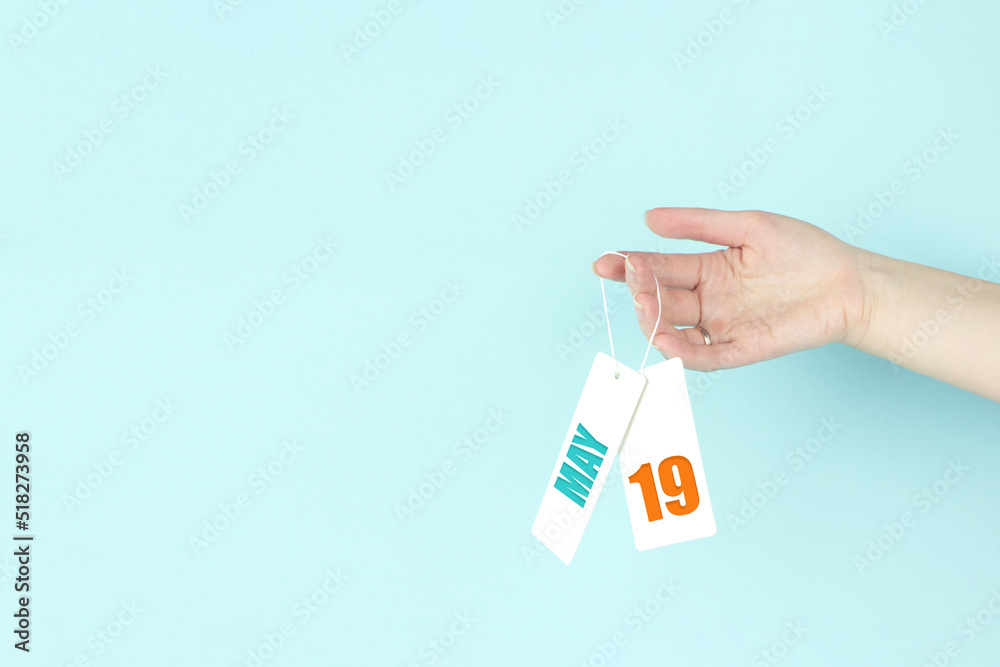 May 19th. Day 19 of month, Calendar date. Hand hold price tag with calendar date on blue background. Spring month, day of the year concept. May 19th. Day 19 of month, Calendar date. Hand hold price tag with calendar date on blue background. Spring month, day of the year concept.
