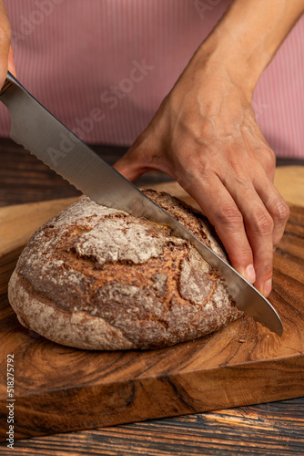 Hands of a woman holding and cutting a rustic sourdough bread with knife - stock photo