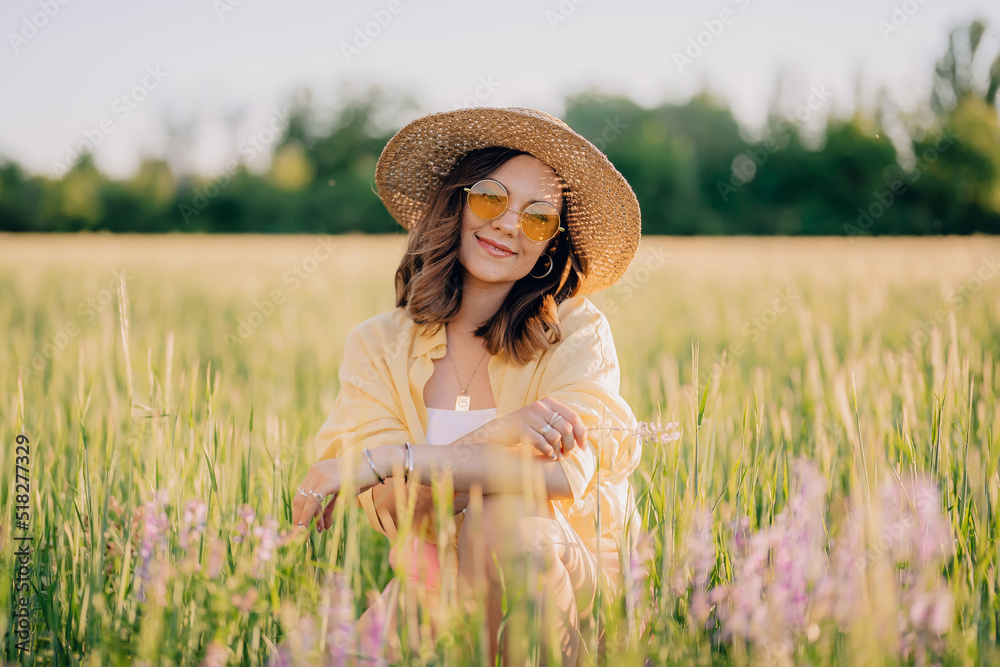 Portrait of rural stylish woman in straw hat posing in fresh wheat field. Grass background. Amazing nature, lifestyle, farmland, growing cereal plants.