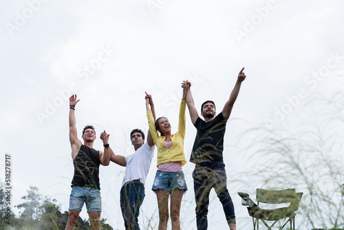 Group of young friends camping standing on mountain and raising up their hands to the air