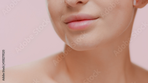 Big close-up shot of young slim white-skinned woman smiles for the camera on pale pink background | Sagging jowls prevention concept