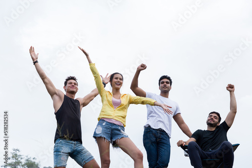 Group of young friends camping standing on mountain and raising up their hands to the air