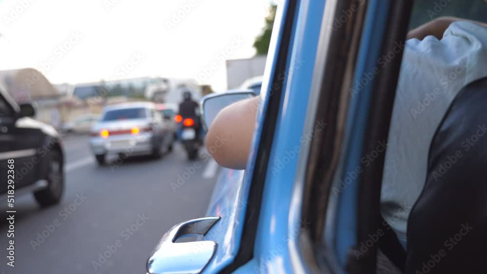View from side to old retro car standing in traffic jam in downtown. Unrecognizable man driving a blue vintage automobile on asphalt road in the city. Rear back view Close up Slow motion