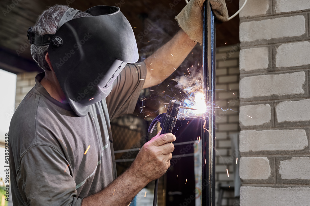 Welder with protective mask welding metal performs welding work