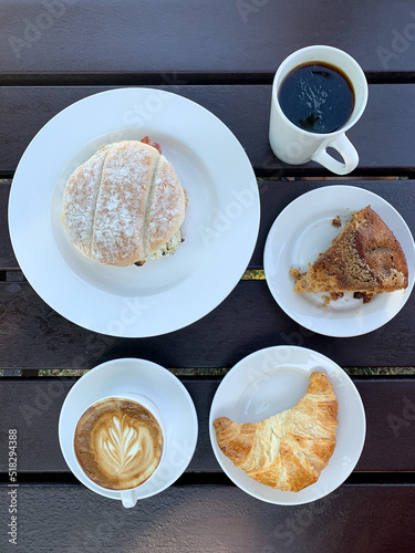 Breakfast in a cafe for two. Directly above. French style breakfast for two in a cafe. Latte art coffee with freshly baked croissant on a black wooden table, Piece of cake, scones, egg and bacon roll.