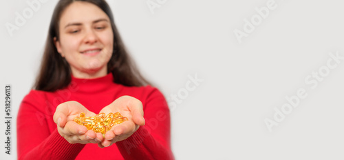A woman smiling holds in her palms a handful of capsules of fish oil  omega 3. Banner with place for text.